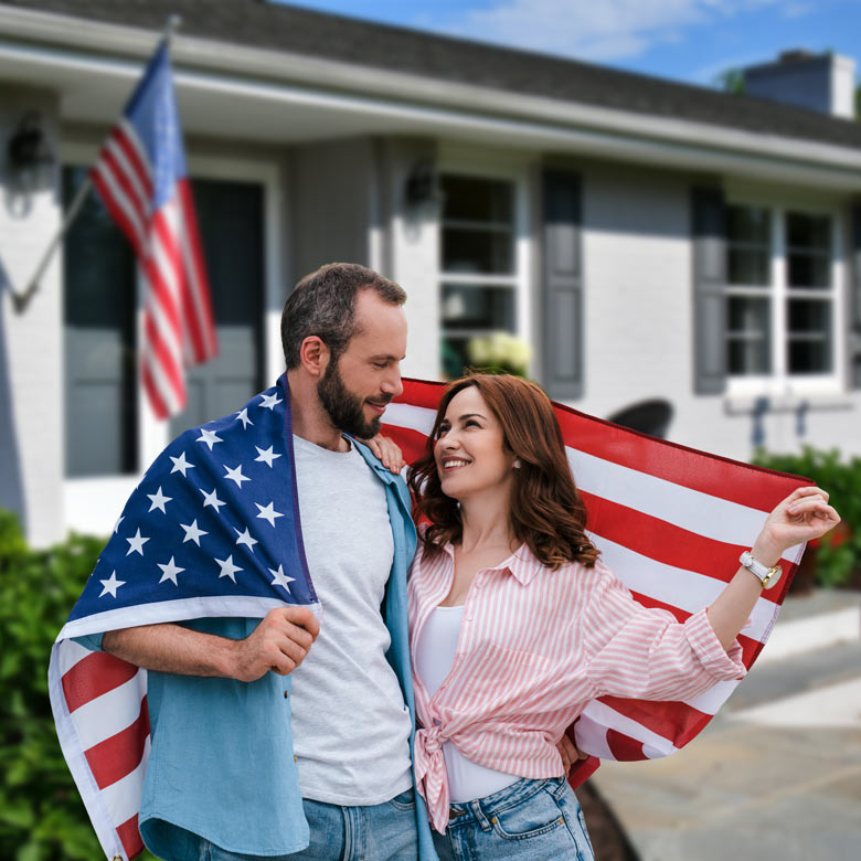 Casal segurando uma bandeira dos Estados Unidos em frente a uma casa